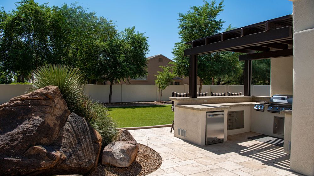 Built-in outdoor kitchen with a grill and counters under a dark pergola (stock photo)