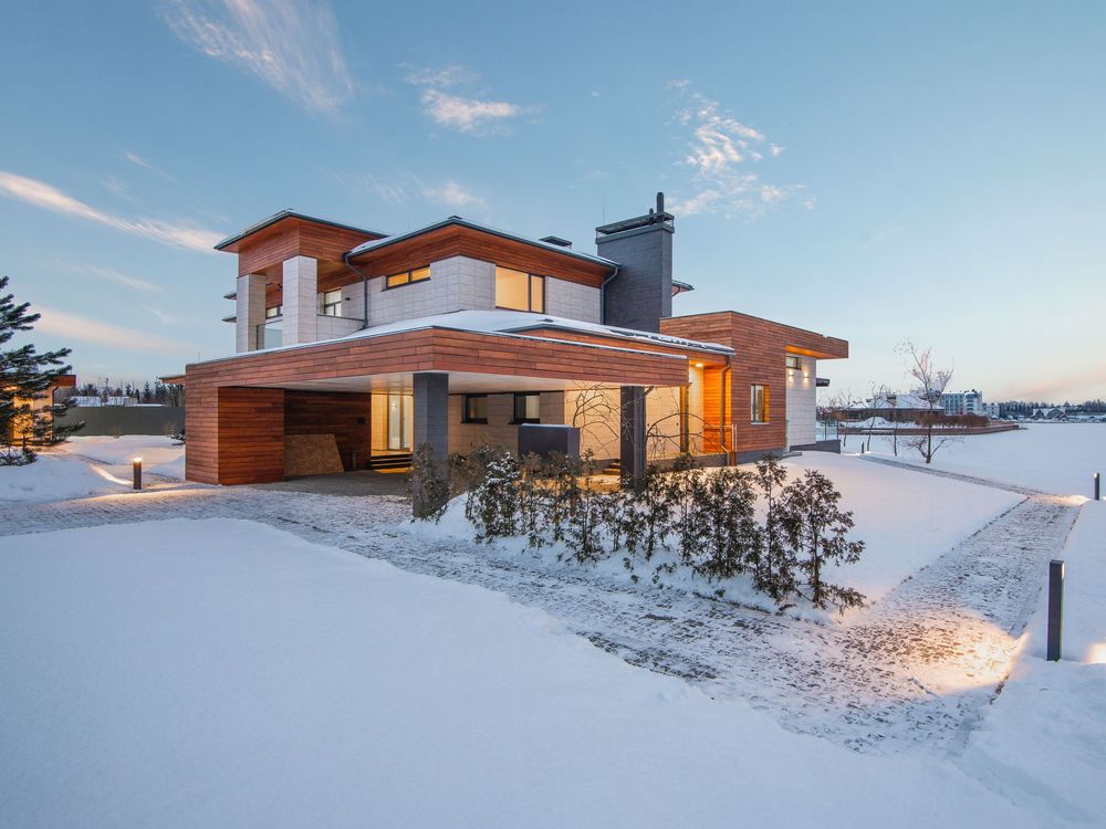 Modern home with a clear, lit walk and drive through fresh snow at dusk (stock photo)
